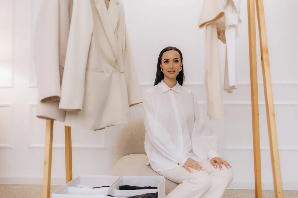 Woman seated beside a rail of pale neutral clothing