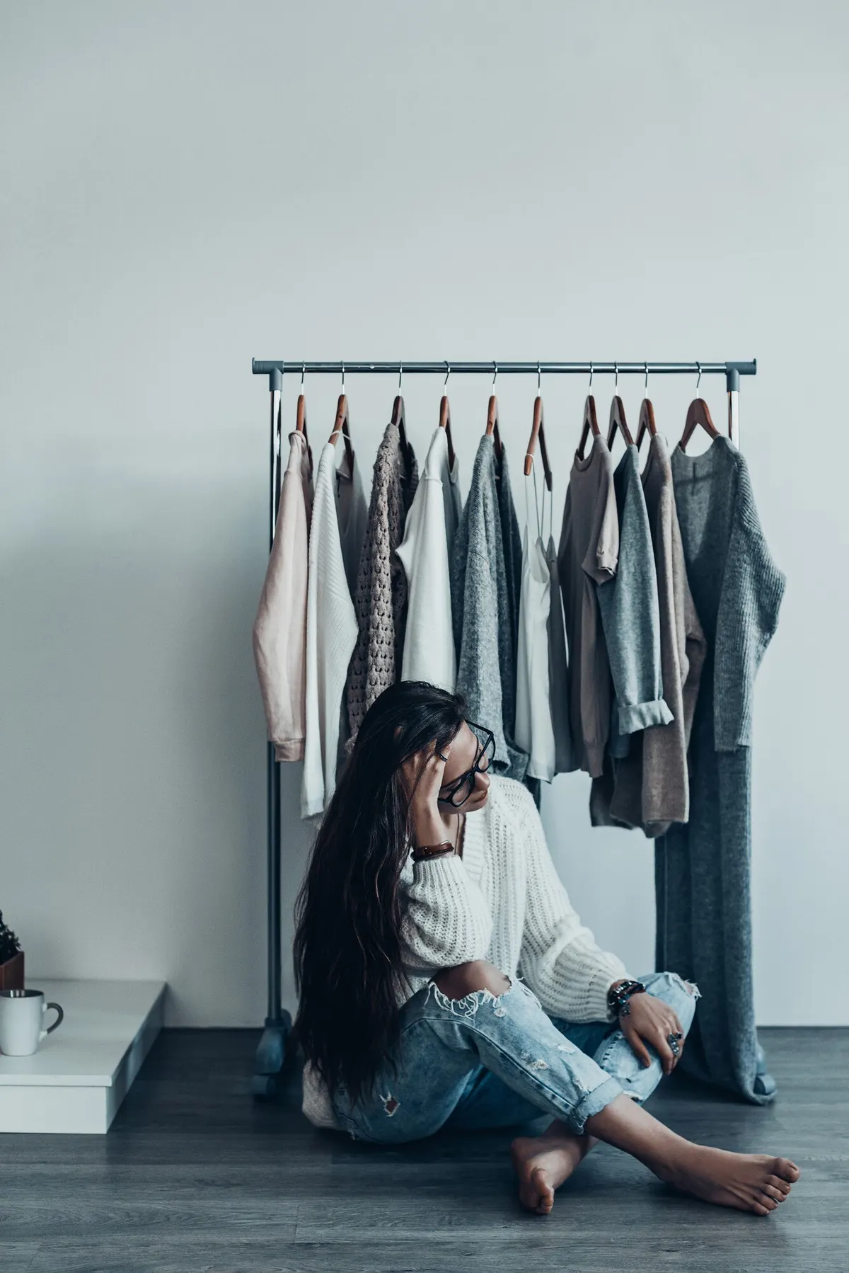 Woman seated beside a small rail of everyday clothing