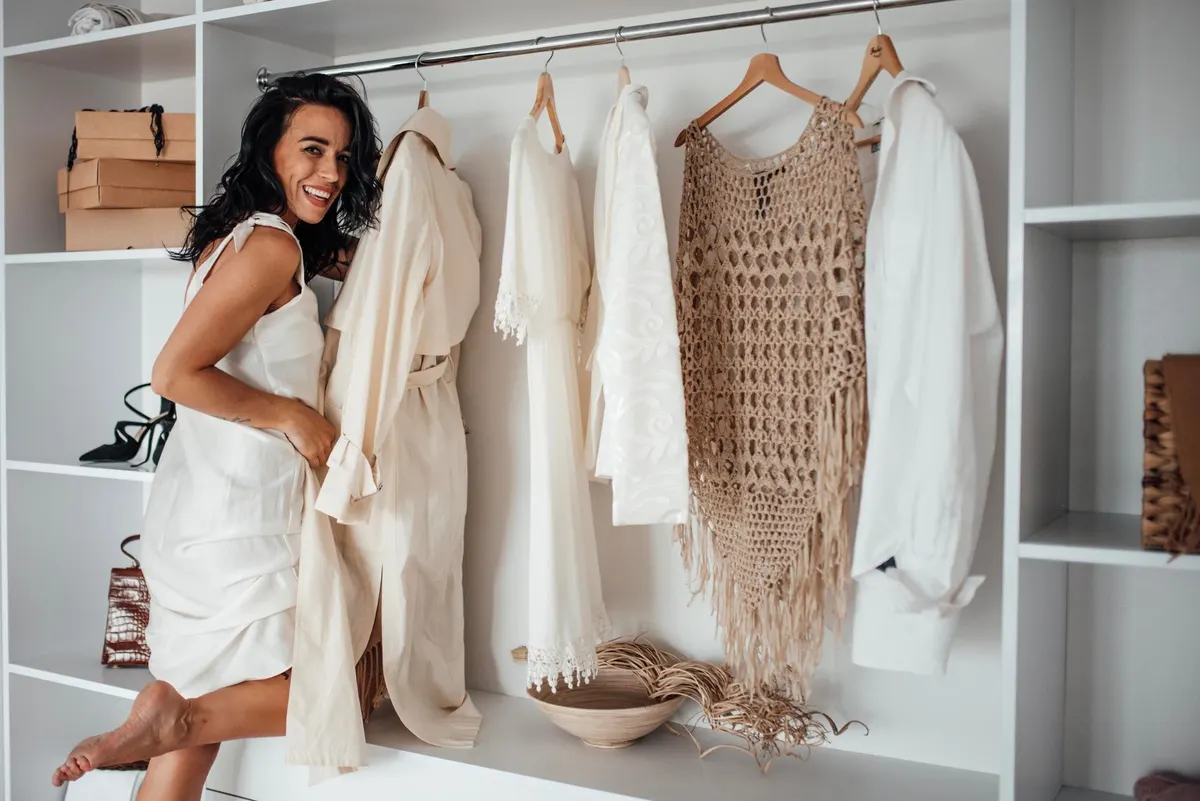 Woman comparing a neutral outfit beside her clothing rail