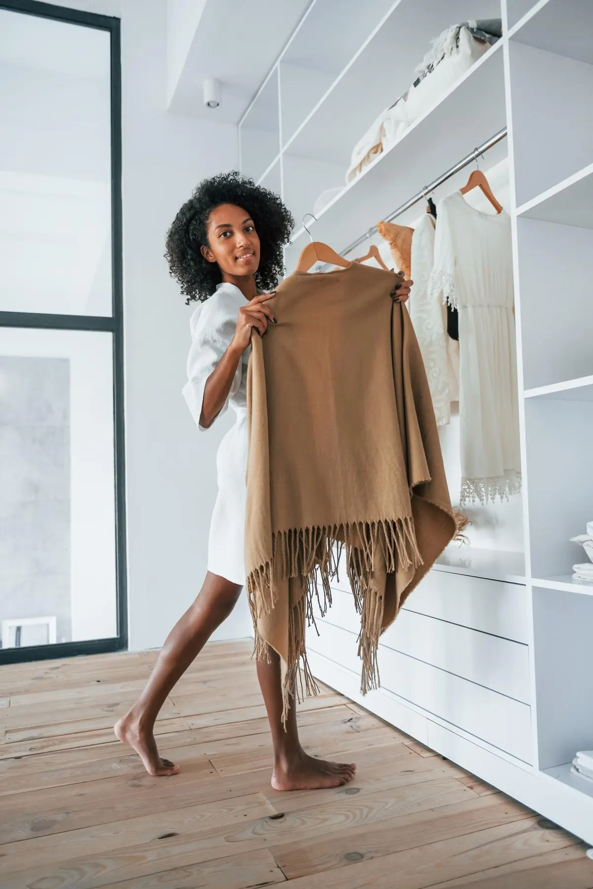 Woman holding up a neutral jacket beside her wardrobe