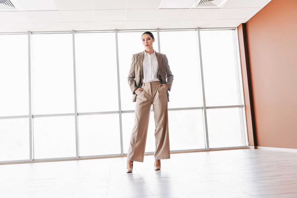 Woman wearing a tailored neutral trouser suit beside a window