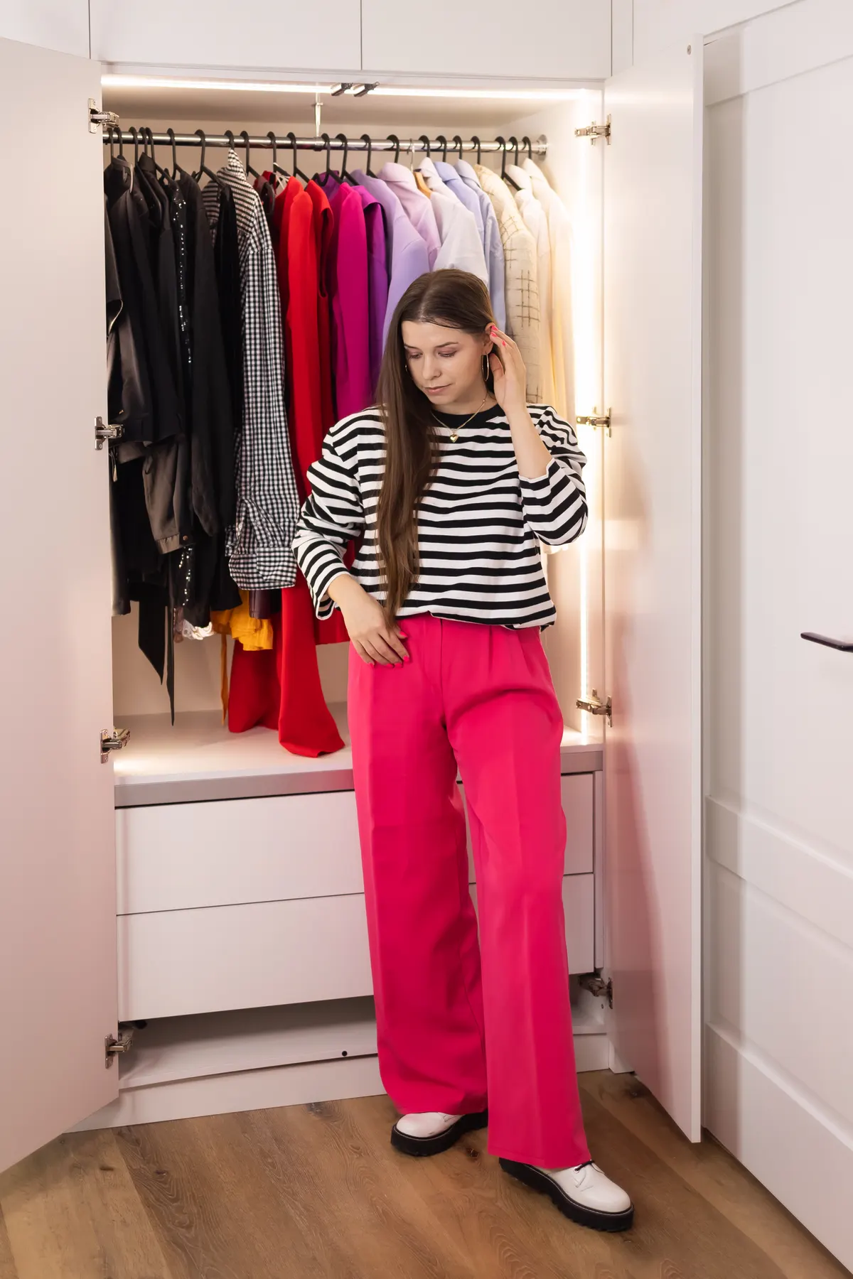 Woman choosing a bright pink outfit beside an open wardrobe